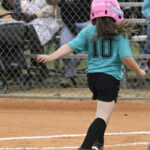 A young girl wearing a teal shirt with the number 10 and a pink helmet runs on a baseball field during a game.