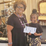 A woman and a young girl smiling and holding a certificate together in a church or event setting.