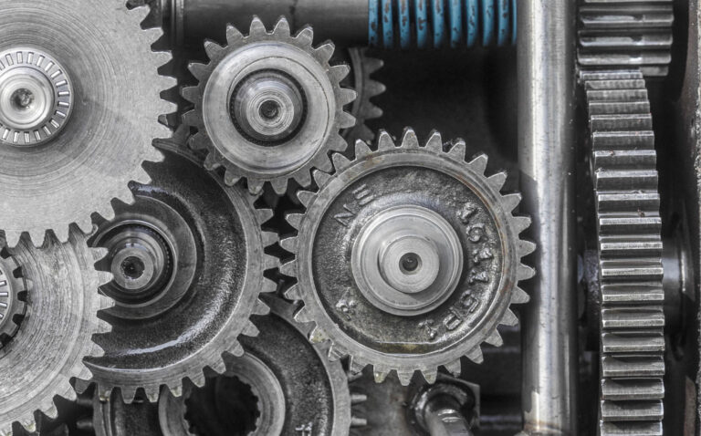 Close-up view of several interlocking metal gears and a visible blue spring inside a mechanical device.