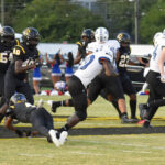 Football players in black and white uniforms are in action on the field during a game, with cheerleaders visible in the background.