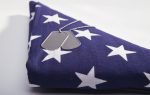 Folded American flag with white stars and a pair of military dog tags resting on top.