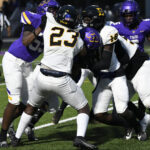Football players in purple and white uniforms clash during a game under bright stadium lights.