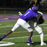 A football player in a purple uniform tackles an opponent in white during a night game on a turf field.