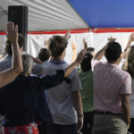 A group of people standing under a tent with their hands raised, participating in an event or gathering.