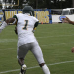 A football player wearing a white uniform with number 1 runs on a field during a game, with another player's arm reaching toward him.