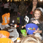 Children in Halloween costumes holding buckets, collecting candy at a festive event.