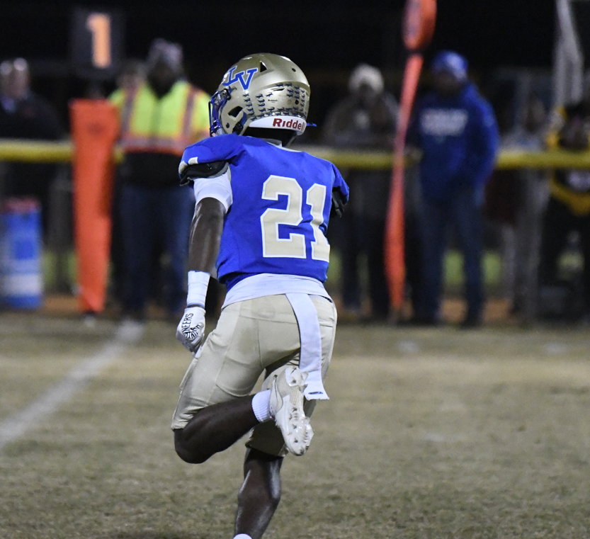 Football player in blue jersey number 21 runs on a field at night, with spectators and officials visible in the background.