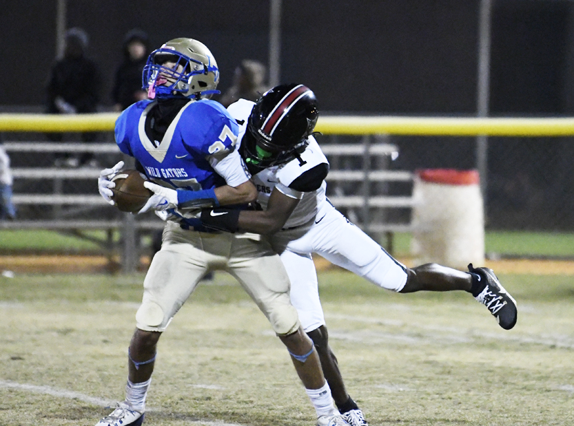 A football player in blue is tackled by an opponent in white during a game on a grassy field at night.