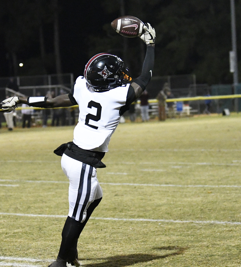 A football player wearing jersey number 2 jumps to catch a football during a nighttime game on a grassy field.
