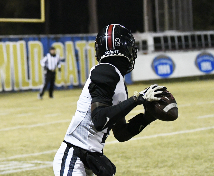 A football player in a black and white uniform prepares to catch a pass during a night game on a field.