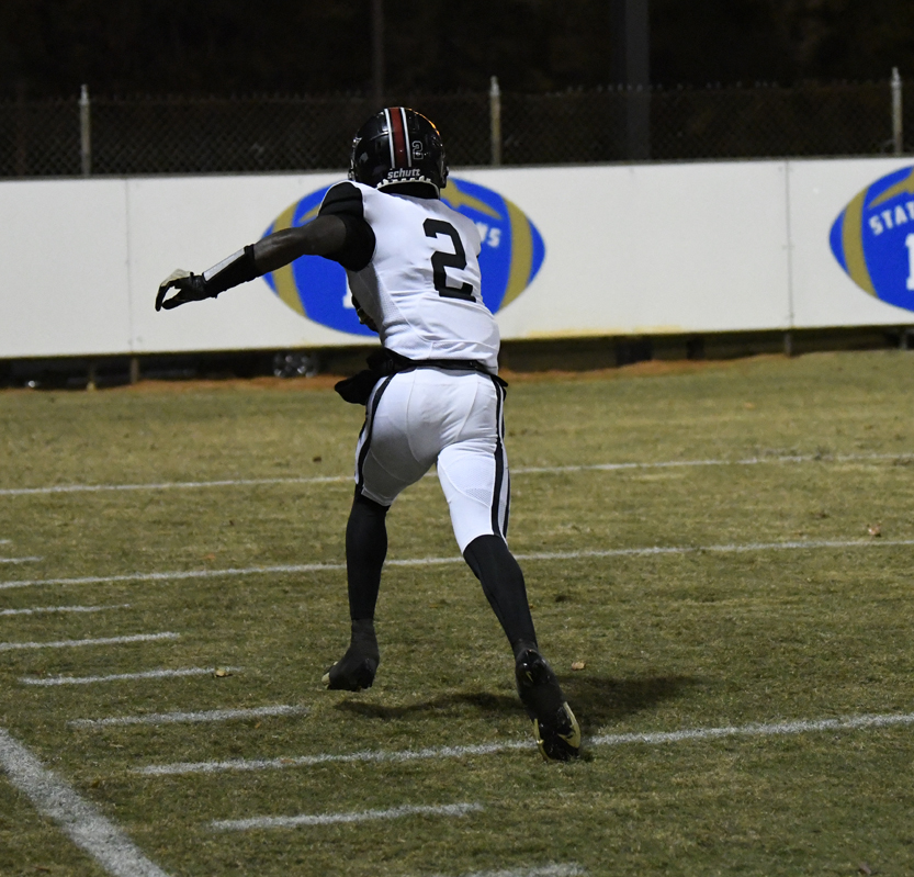 American football player wearing number 2 runs on a field at night, preparing to throw a football. The player is dressed in a black and white uniform.