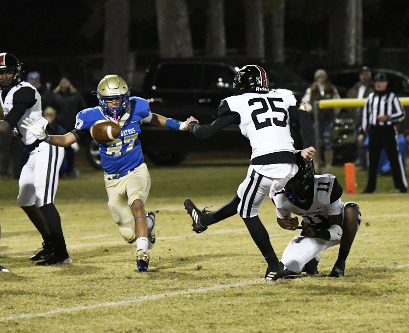 A football player in blue runs with the ball while dodging defenders in black and white uniforms during a nighttime game.