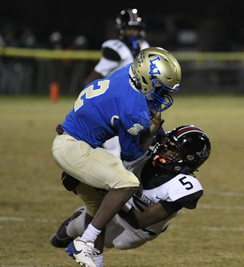 A football player in blue tackles a player in white and black during a night game on a grassy field.