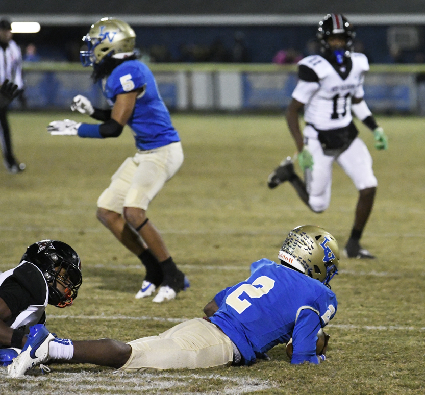 Football players in blue and white uniforms are on a grassy field during a game, with one player lying on the ground after a play.