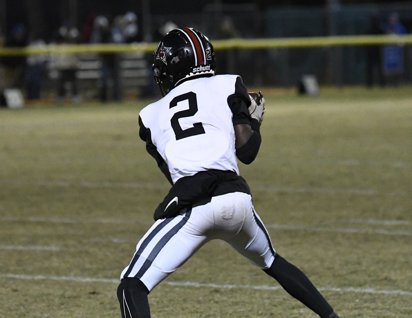 Football player wearing number 2 jersey prepares to throw the ball during a nighttime game on a grassy field.