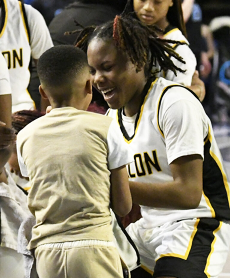 A basketball player in a white uniform smiles and interacts joyfully with a young child on the court after a game.