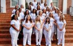 A group of people dressed in white uniforms posing on steps in front of a brick building with columns.