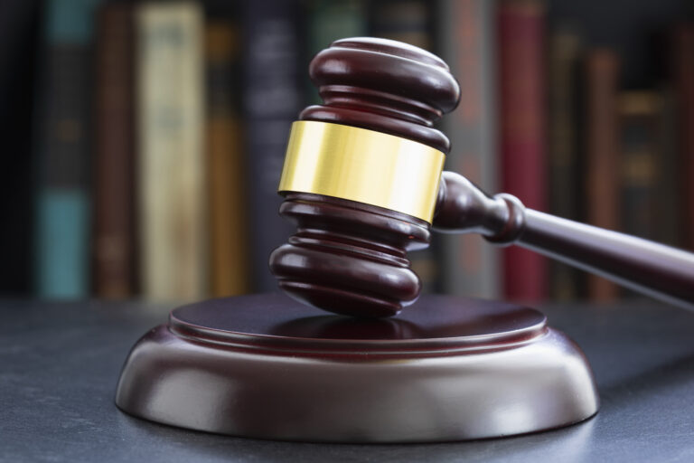 A judge’s wooden gavel resting on a sound block with blurred law books in the background.