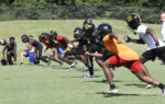 A group of young football players in helmets and sportswear practice running drills on a grassy field during daytime.