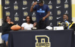 A student athlete puts on a cap at a signing event, with family beside him and a Dillon High School banner in the background.