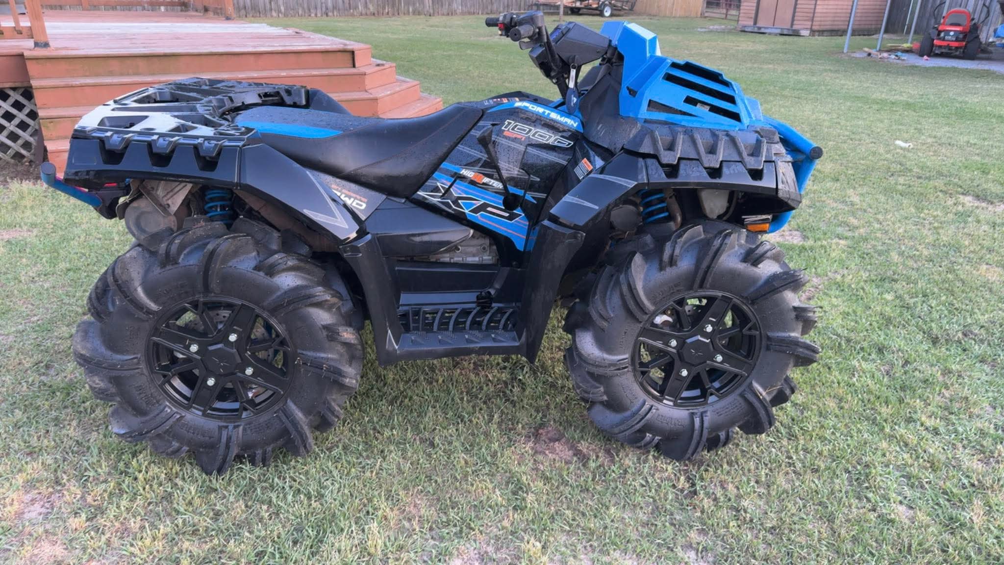 A blue and black all-terrain vehicle (ATV) with large, rugged tires parked on grass near brick steps.