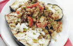 Grilled eggplant slices topped with a mixture of rice, vegetables, and herbs on a white plate, placed on a red napkin.