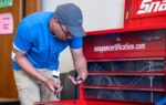 A man in a blue shirt works with tools near a red tool chest labeled "snaponcertification.com" in a workshop setting.