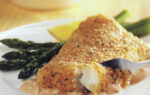 A breaded fish fillet served with asparagus and a slice of lemon on a white plate, with a fork cutting into the fish.