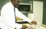 A man in a white shirt and tie is carving or serving food on a table in a room.