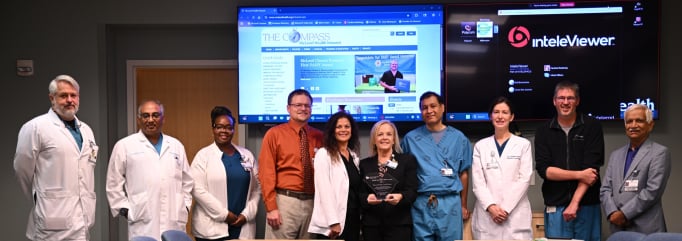 Five professionals pose together indoors, with a large computer screen displaying a website in the background.