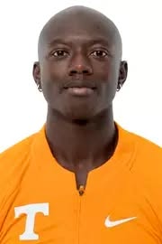 A person with short hair wearing an orange shirt, looking directly at the camera against a plain white background.