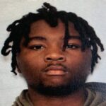 A young man with short dreadlocks looking at the camera, neutral expression, against a plain background.