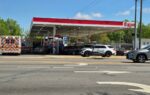 A gas station with several cars at the pumps, including a police vehicle, on a sunny day.