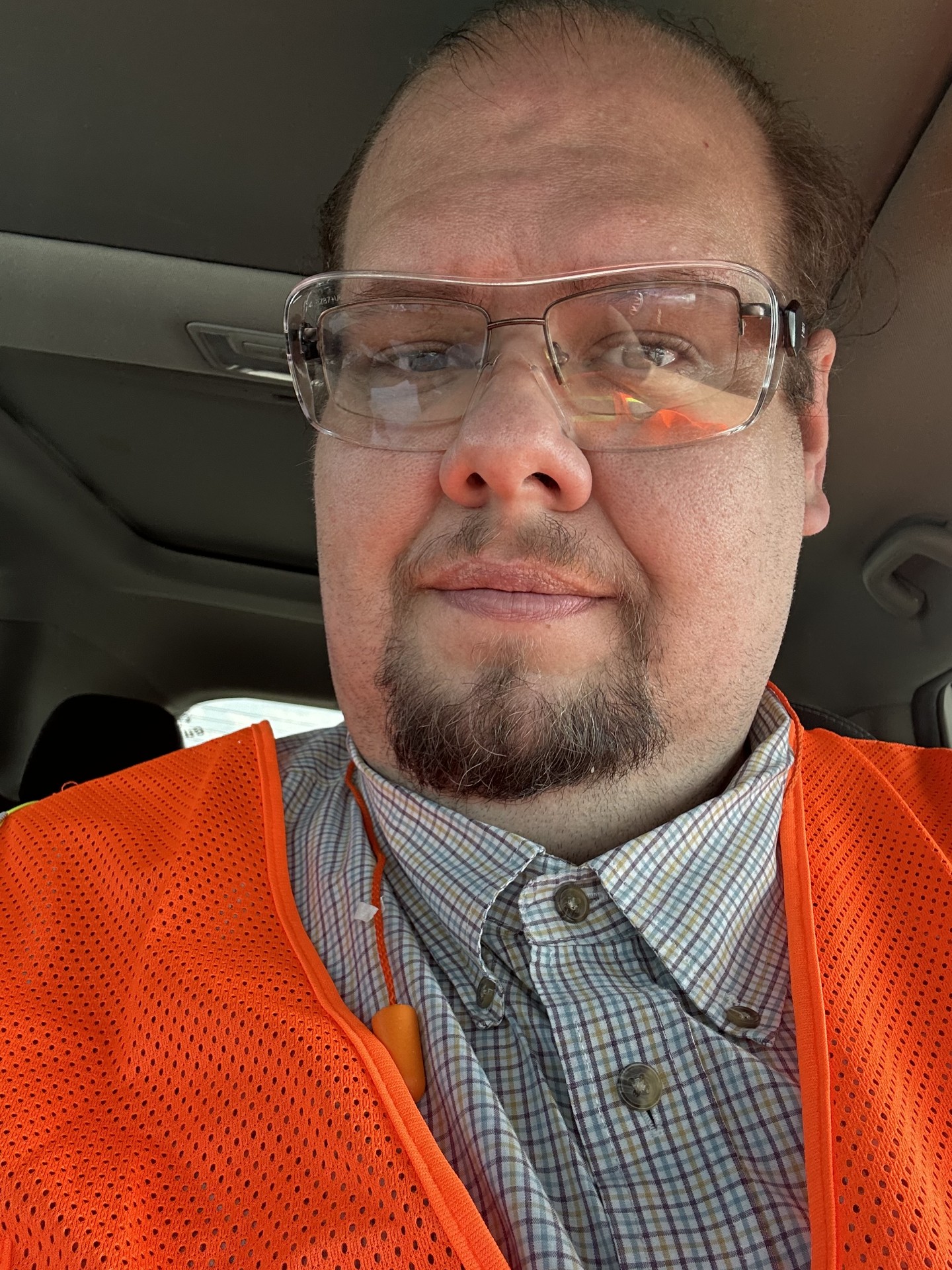 Man wearing safety glasses and an orange safety vest, sitting inside a vehicle.