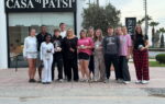 A group of people standing together on a sidewalk in front of a building with a sign reading “SA DI PATSI.”