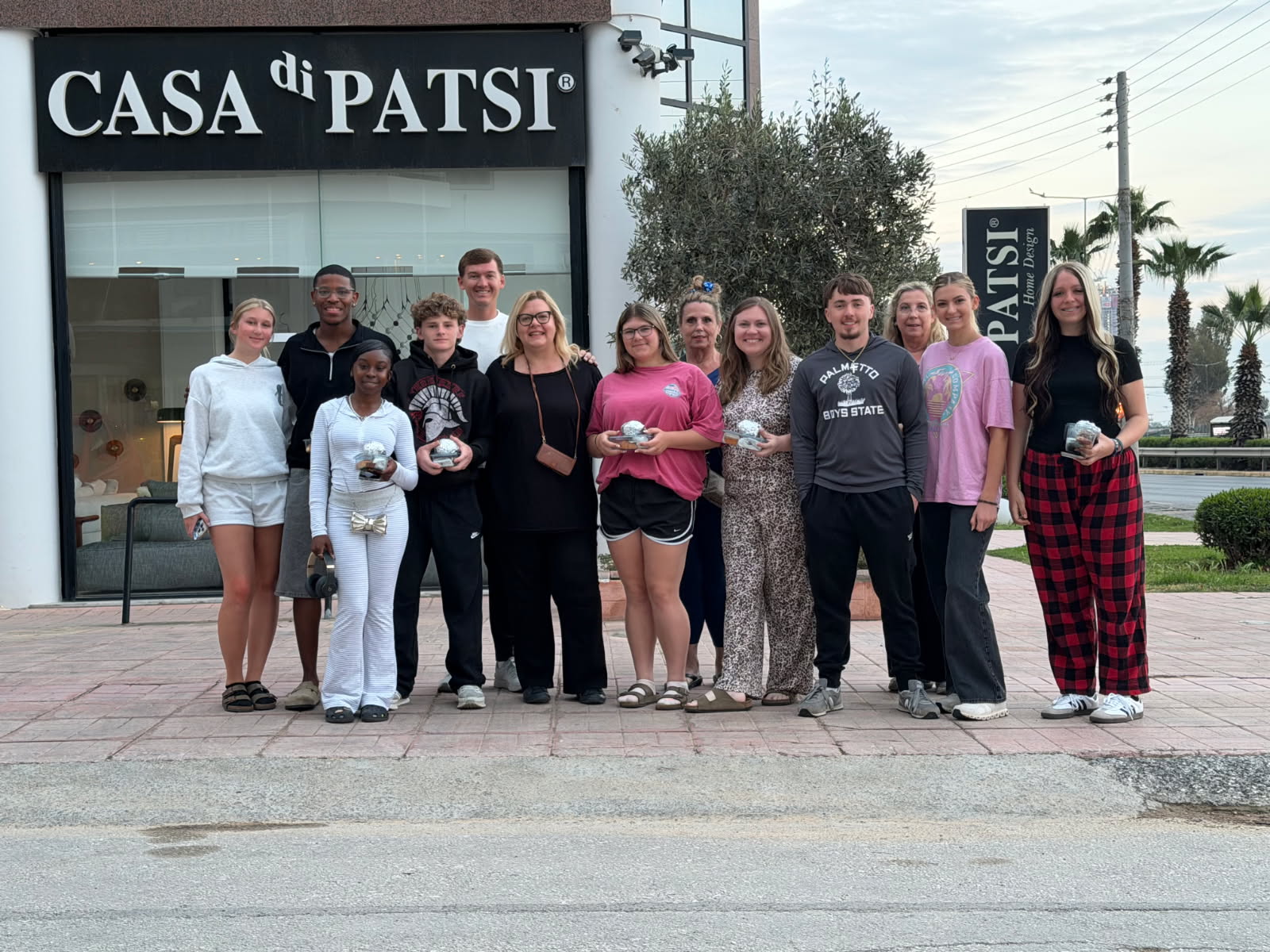 A group of people standing together on a sidewalk in front of a building with a sign reading “SA DI PATSI.”