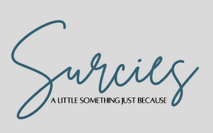The text "Surcie" in cursive script with the tagline "A little something just because" on a light gray background.