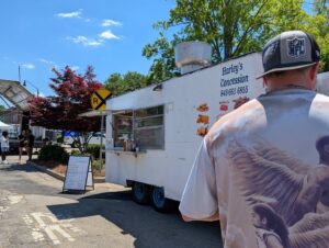 A man stands in front of Harley's Concession food truck with a visible menu board outside on a sunny day.