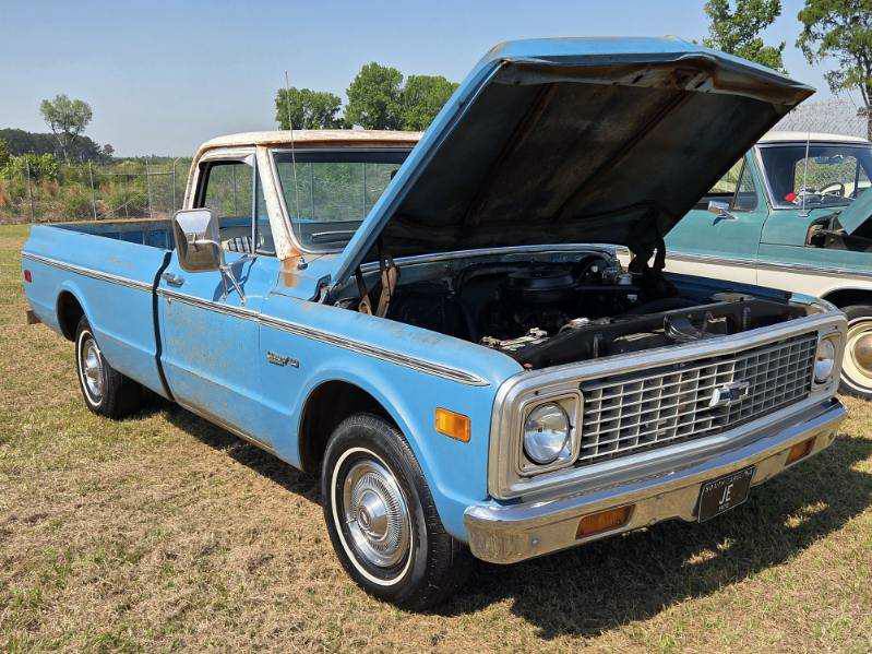 A vintage blue pickup truck with its hood open, parked outdoors on grass under a clear sky.