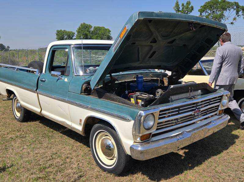 A vintage light blue and white pickup truck with its hood open, parked on grass at a car show.