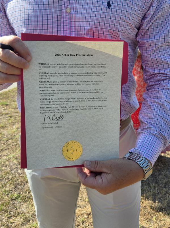 A person holding a 2026 Arbor Day Proclamation document with an official gold seal, wearing a plaid shirt and standing outdoors.