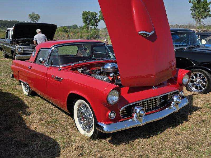 A classic red car with its hood open is displayed outdoors on grass during a car show.