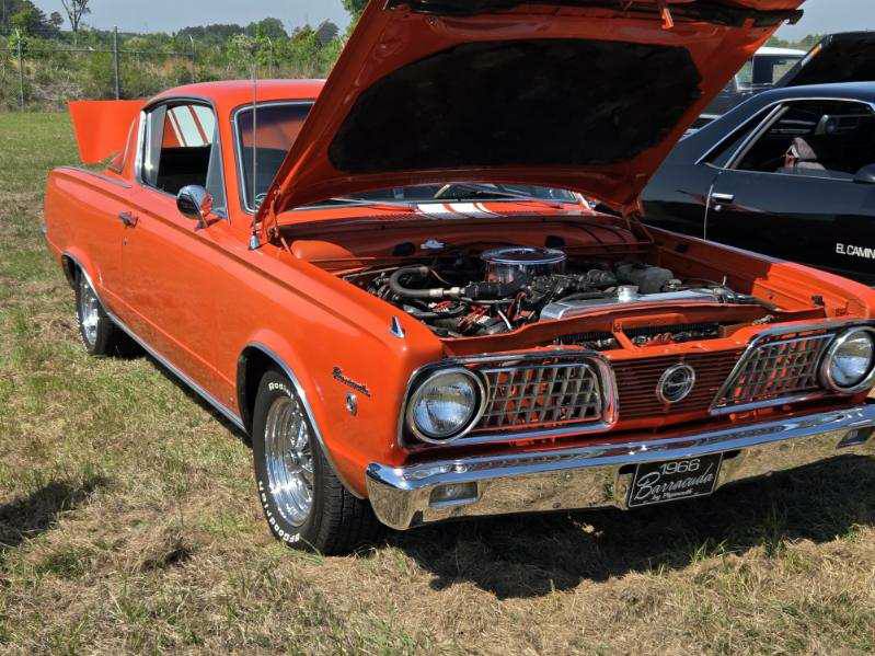 orange vintage car with its hood open, showcasing the engine, parked on grass at an outdoor event.