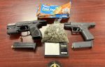 Two handguns, magazines, a bag of marijuana, a digital scale, sandwich bags, a sheriff’s badge, and bullets laid out on a wooden table.