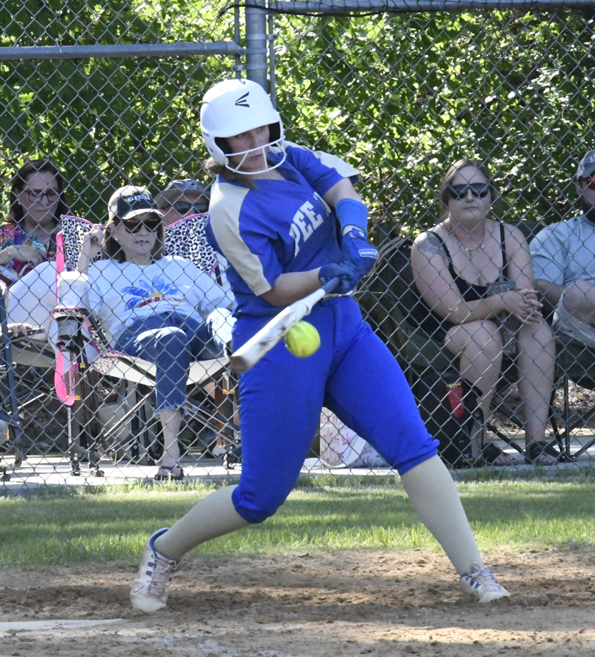 Softball player in blue uniform hitting a yellow softball, with spectators sitting behind a fence in the background.