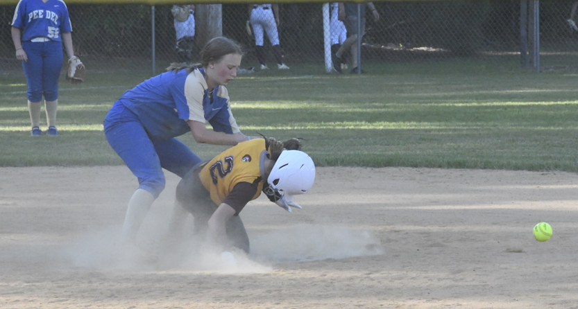 A softball player in yellow slides into base while a player in blue attempts to tag them, dust rising from the ground.