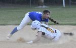 Two softball players in action; one in blue attempts to tag out a sliding player in white uniform and helmet on a dusty infield.
