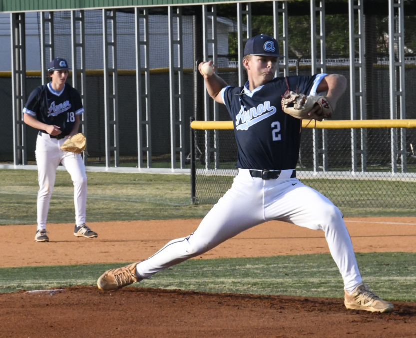 Baseball pitcher in blue and white uniform winds up to throw, while another player stands ready in the background on the field.