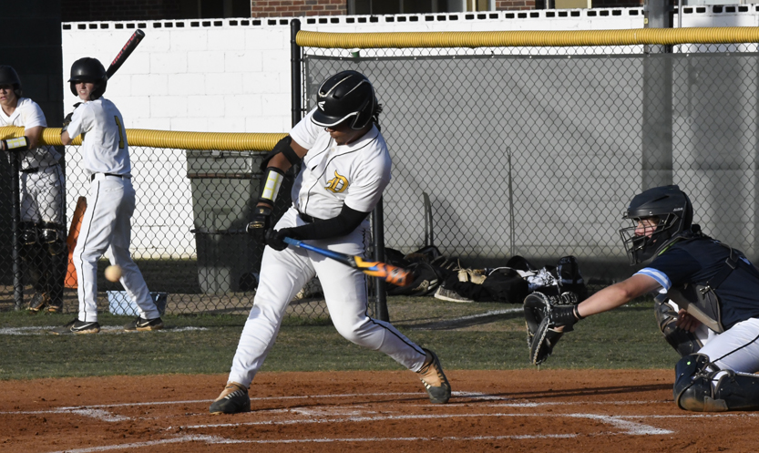 Baseball player in white uniform swinging bat at pitched ball, catcher in dark gear ready to catch, other players and fence in background.