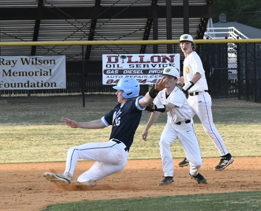 Baseball player in blue sliding into base as two players in white prepare to make a play during a game.
